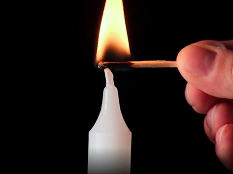 Ein Streichholz entzündet eine Kerze.